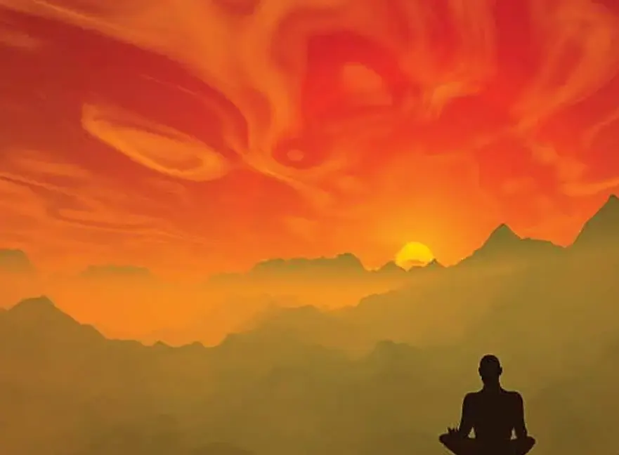 Person meditating in silhouette facing a dramatic orange and golden sunset over mountains.