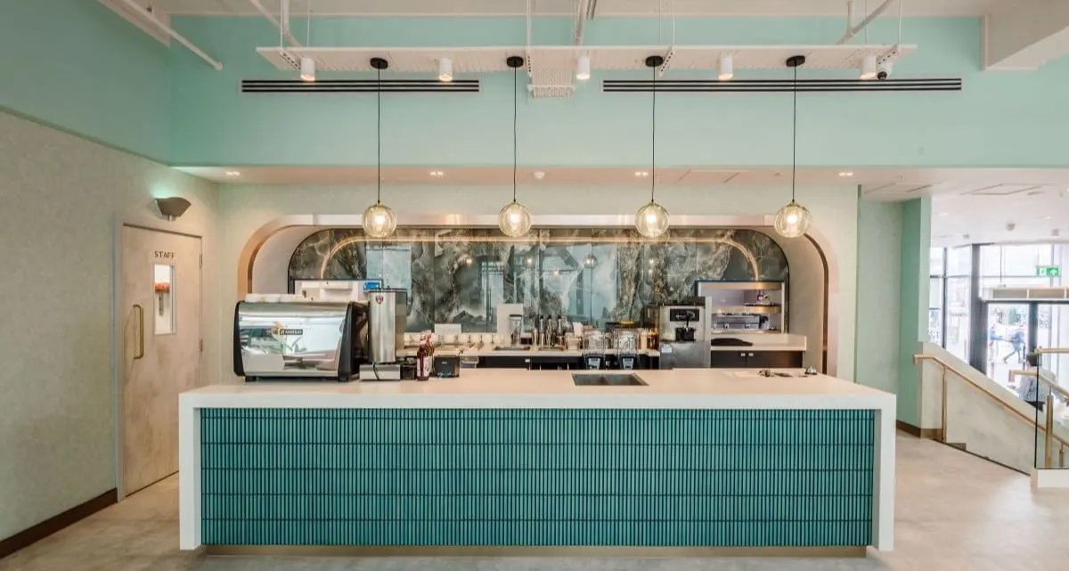 Modern reception desk with turquoise panelling, pendant lights, and staff member behind counter in contemporary leisure venue interior.