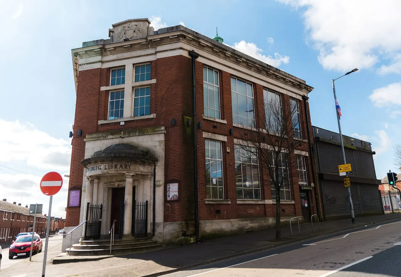 Victorian red-brick library building with classical portico entrance on a street corner under blue sky.