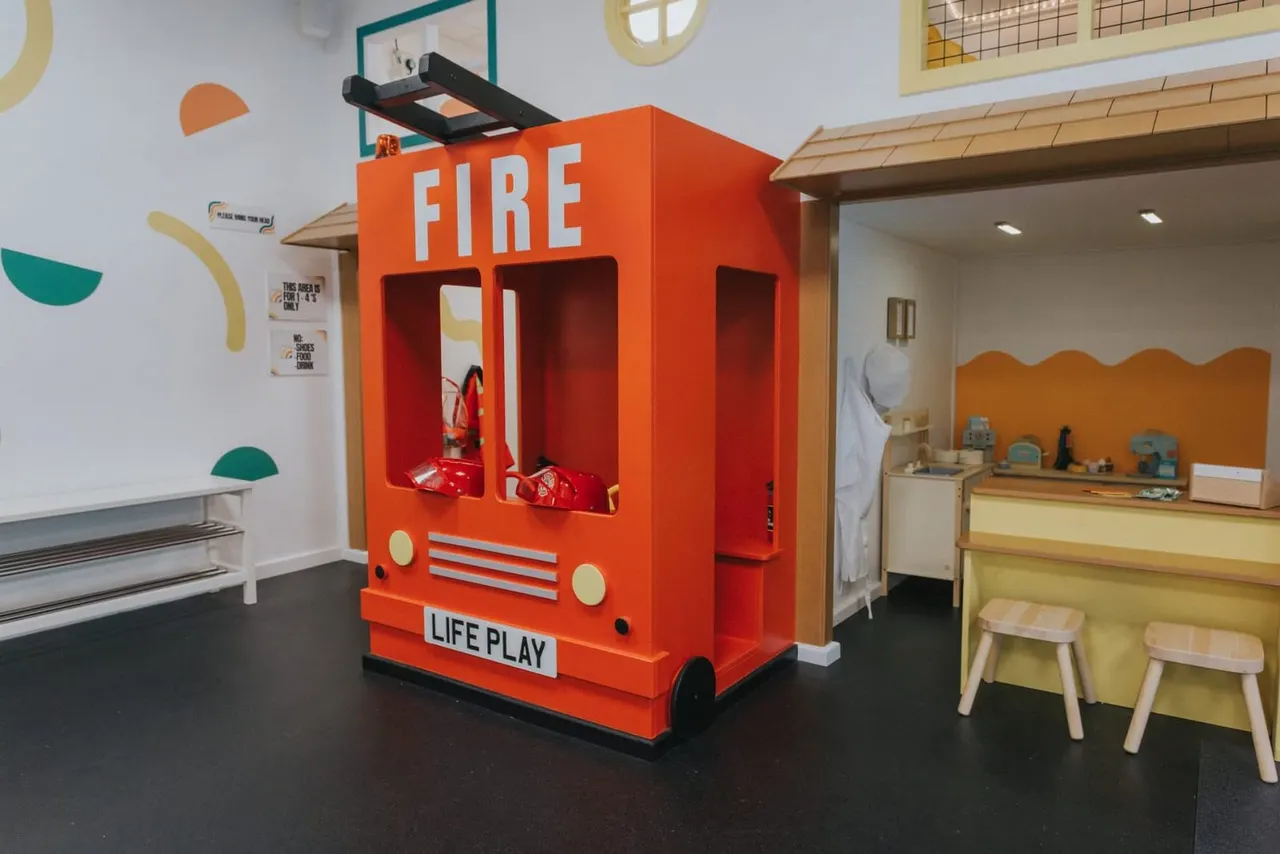 Bright indoor play area with a large red toy fire engine and colourful wall decorations in a soft play facility.