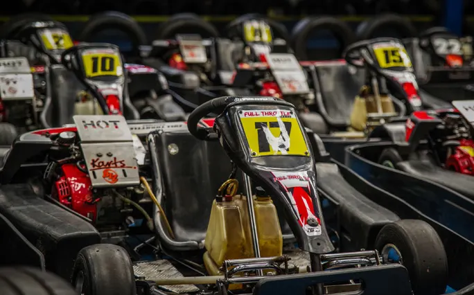 Row of numbered go-karts lined up at an indoor racing venue, with focus on a gold and white kart in the foreground.