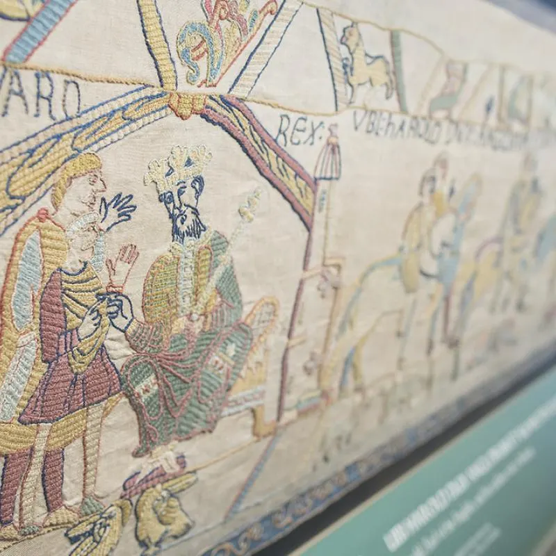 Close-up of embroidered medieval tapestry showing figures in period dress and decorative borders.
