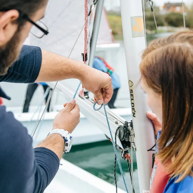 Man and child learning to tie sailing knots on a boat during a sailing lesson.