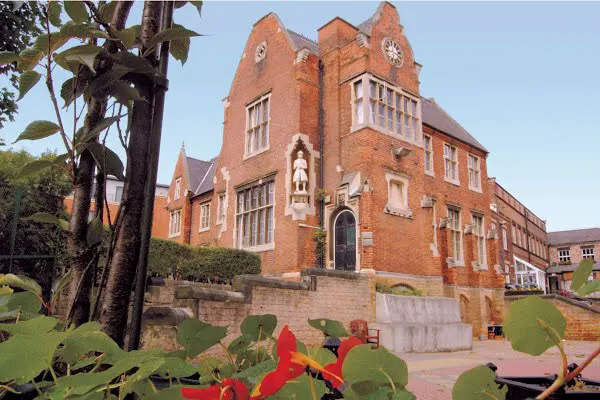 Victorian red brick building with clock tower and manicured gardens in foreground.