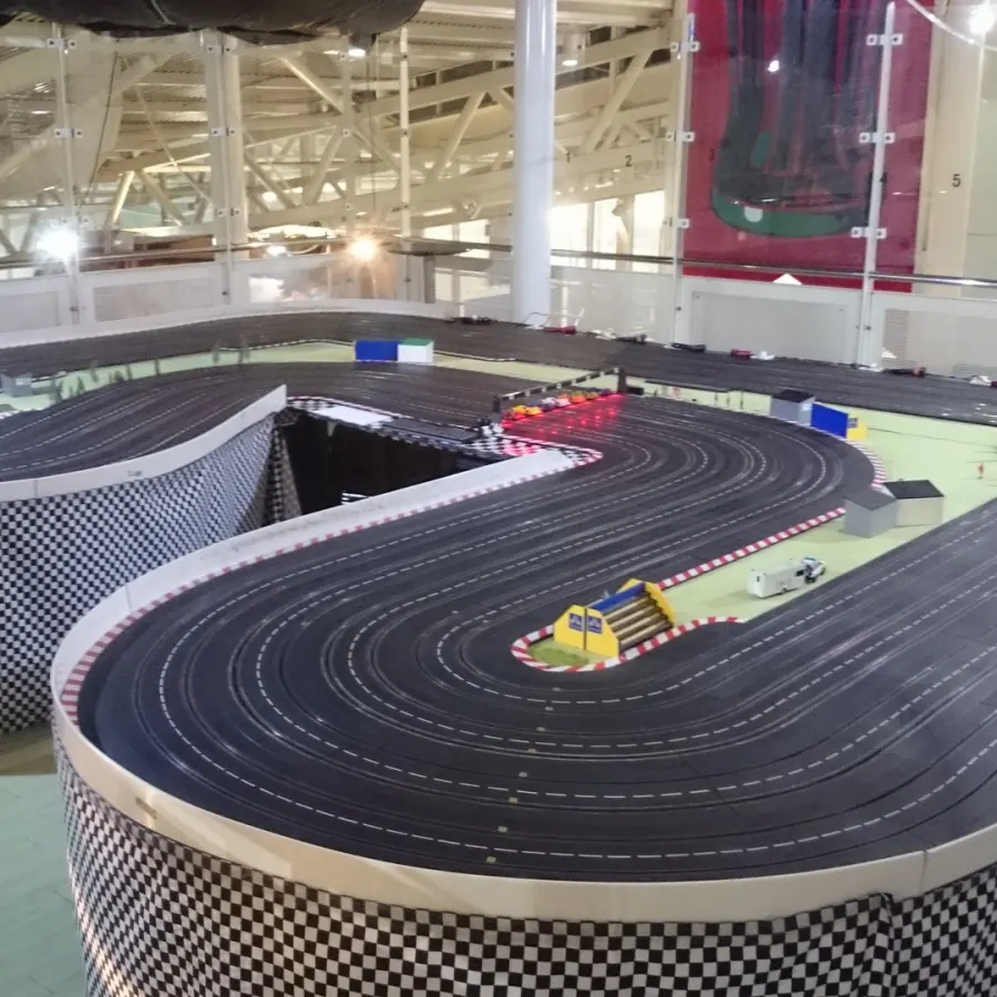 Indoor slot car racing track with miniature cars on a multi-lane circuit in an industrial venue.