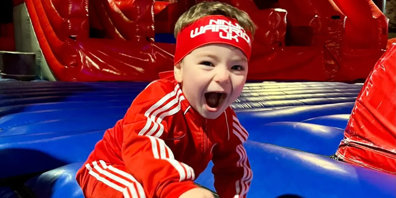 Young child smiling excitedly inside a red inflatable obstacle course structure.