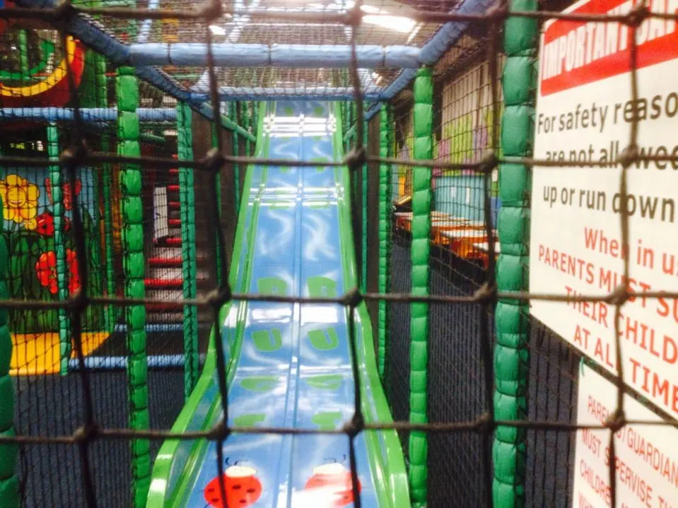 A view down a green and black inflatable play tunnel with safety netting, leading towards daylight.