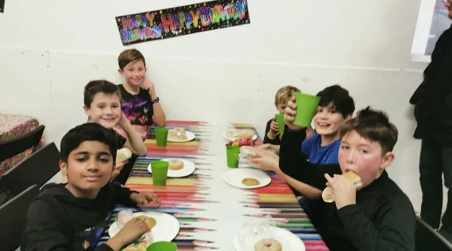 A group of children eating food at a colourful table during a party or event.