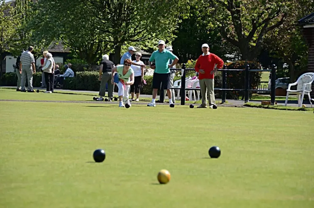 Players and spectators enjoying bowls on a sunny green at an outdoor leisure facility.