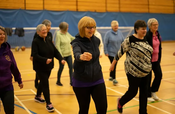 Group of adults of various ages jogging together in a sports hall during an exercise class.