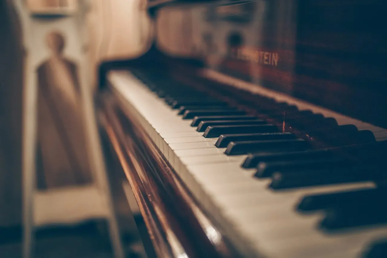 Close-up of piano keyboard with blurred figures in background.