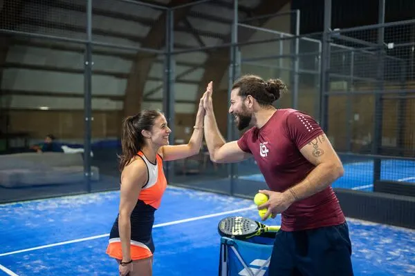 A man and woman high-five on an indoor paddle tennis court after playing together.