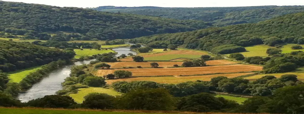 River winding through a lush valley with patchwork agricultural fields and dense woodland.
