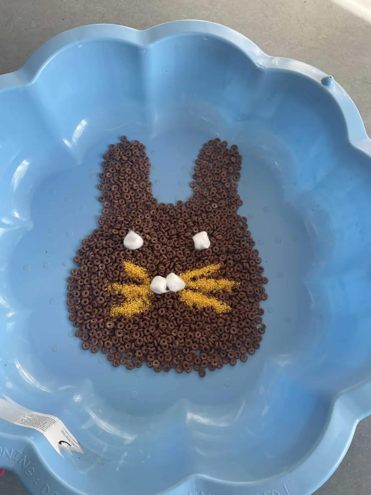Chocolate cereal arranged in a bunny face shape with white and gold decorative details in a blue plate.