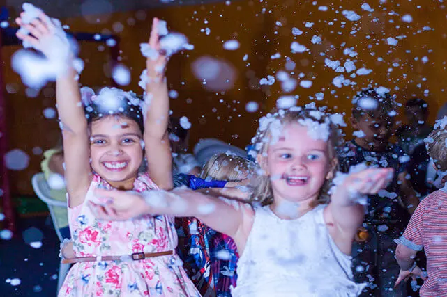 Young children enjoying confetti falling around them whilst playing indoors.