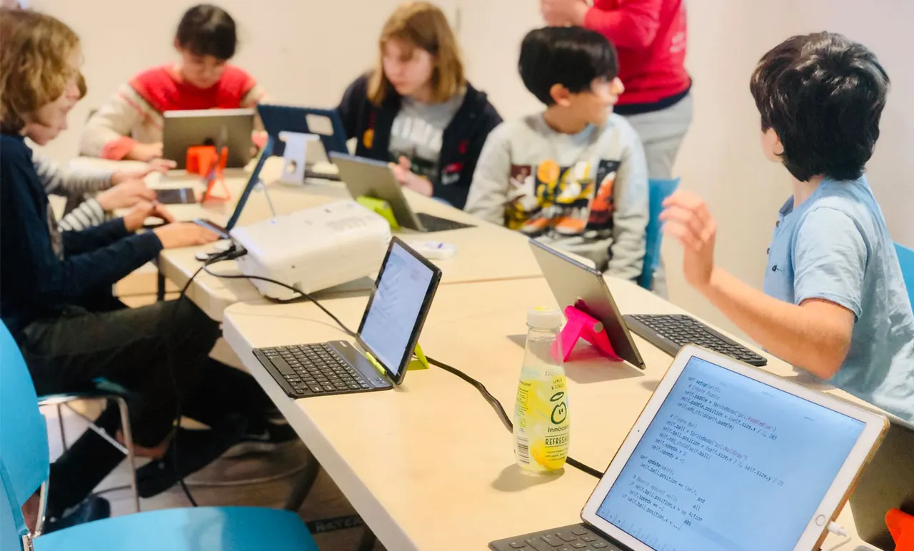 Children seated around a table with laptops during a coding or computer learning class.