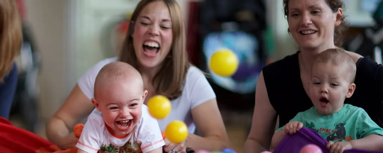 Two women with young toddlers playing with coloured balls in an indoor soft play area.