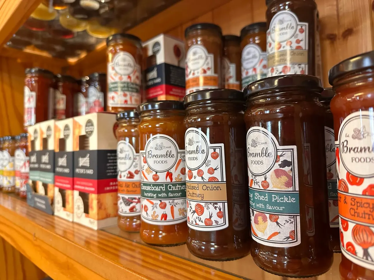 Jars of Bramble Foods preserves and chutneys displayed on wooden shelves in a shop.