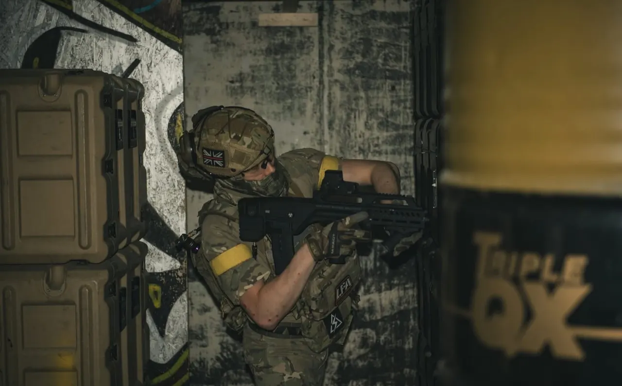 Person in military-style camouflage and helmet holding an airsoft rifle in an indoor arena with weathered walls.