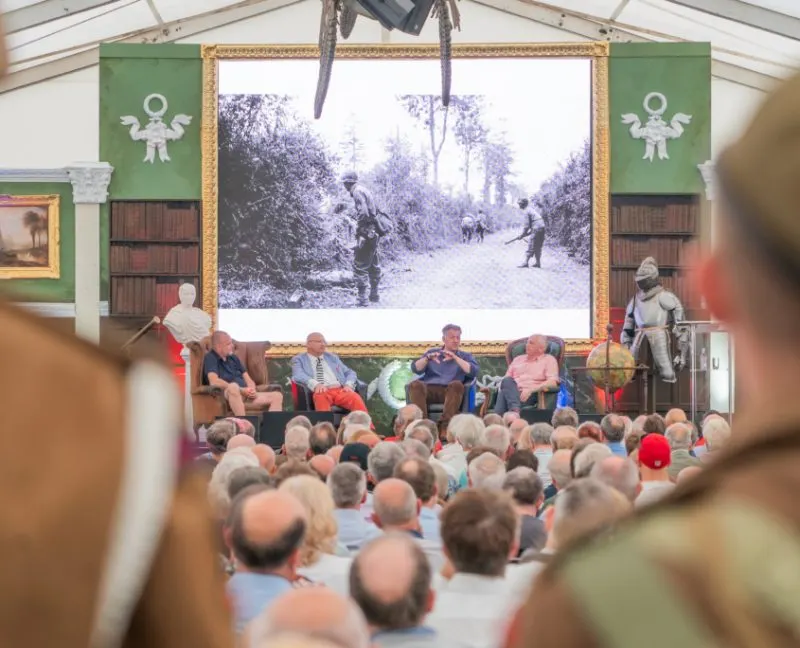 Audience watching a panel discussion with a large historical photograph displayed behind the speakers in a marquee tent.