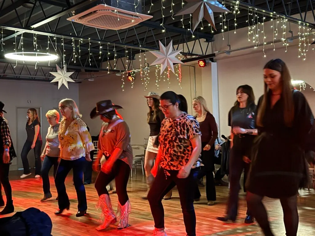 Group of adults dancing and socialising in a decorated indoor venue with festive lights and large stars hanging from the ceiling.