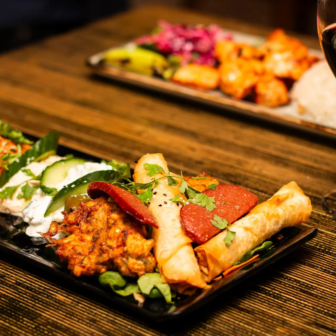 Plated Asian appetisers including spring rolls, spiced meat and vegetables with fresh herbs on wooden table.