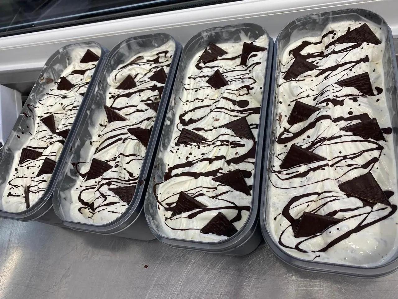 Four clear containers of chocolate and vanilla swirl ice cream displayed in a freezer case.