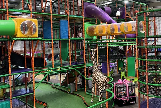 Children playing in a multi-level indoor soft play structure with tunnels, slides and climbing frames in bright colours.