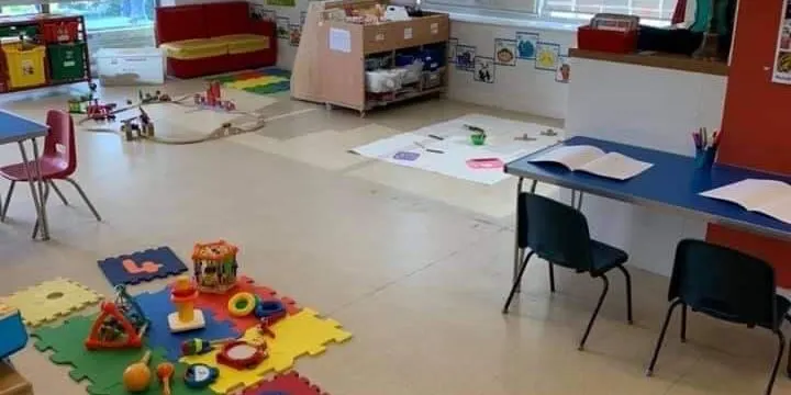 A bright children's activity room with colourful foam play mats, tables with art supplies, storage units and red seating areas.