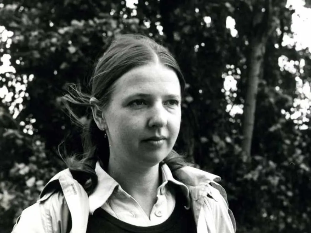 Woman in white shirt stands outdoors among trees in black and white photograph.