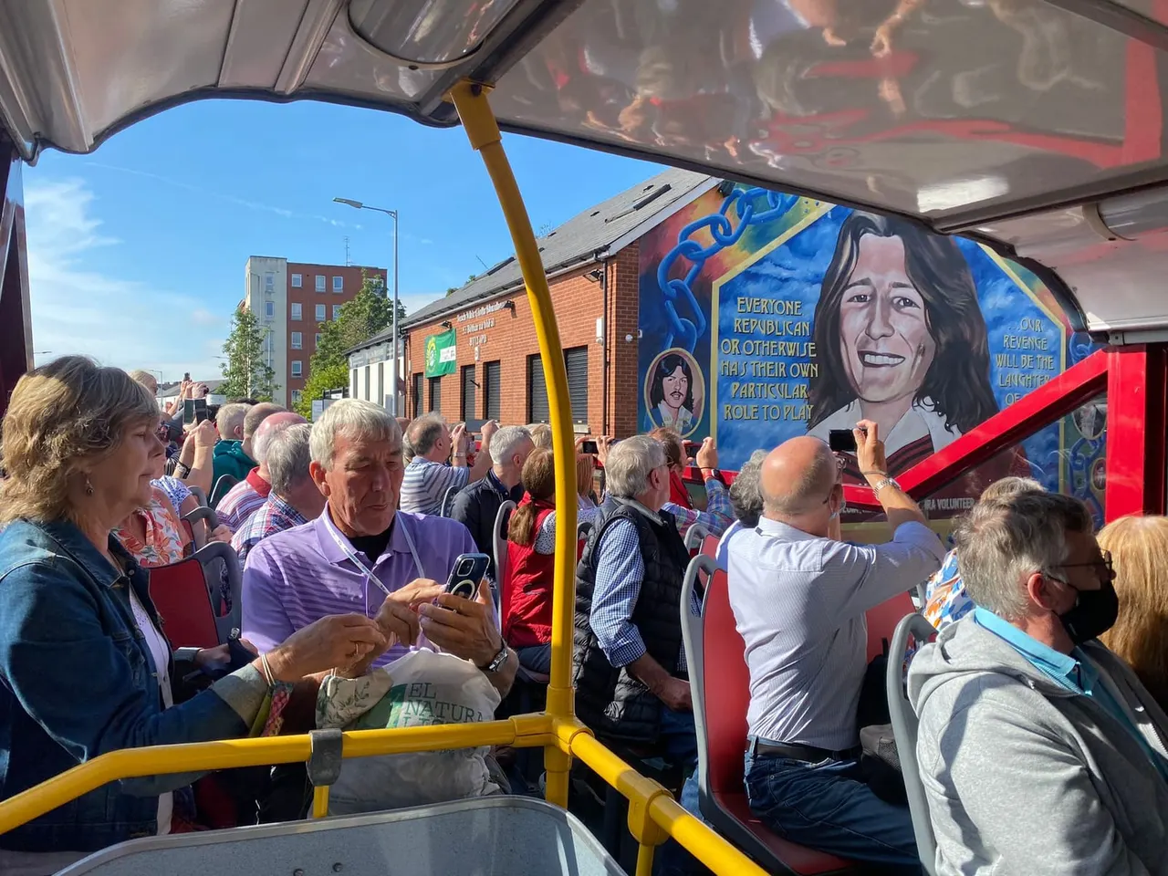 Tourists on an open-top bus tour viewing street murals in an urban area with historic brick buildings.