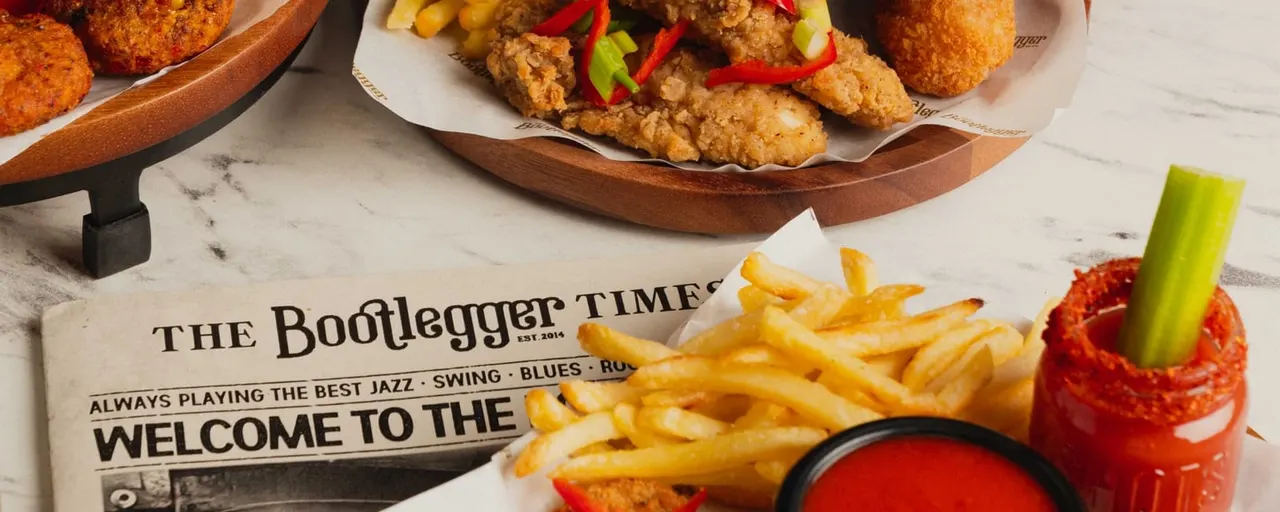 Fried chicken, chips and cocktails arranged on a marble table with a newspaper.