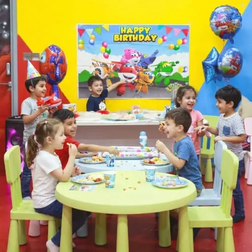 Children eating at a table during a birthday party in a colourful indoor play venue.