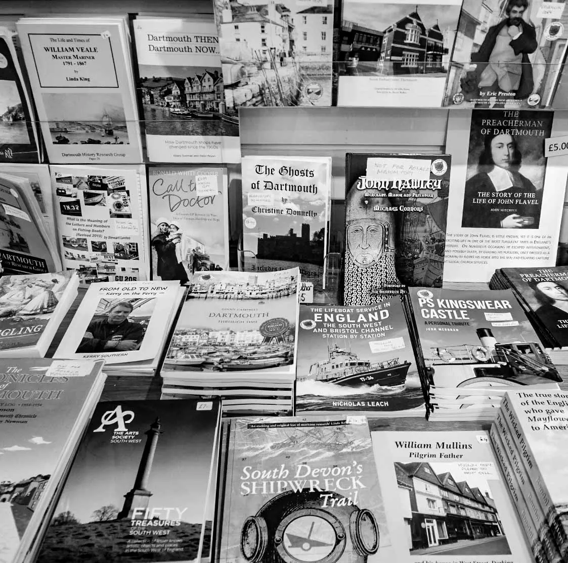 Collection of black and white books and pamphlets about Dartmouth's history, displayed on shelves and tables.