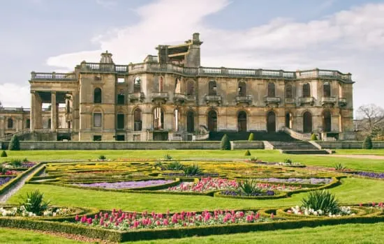 Eighteenth-century stately home with formal gardens featuring flower beds and manicured lawns in front.
