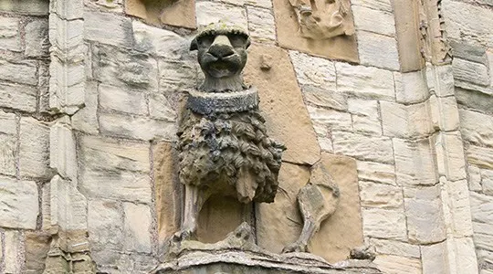 Stone carved owl gargoyle mounted on a pale stone castle wall.