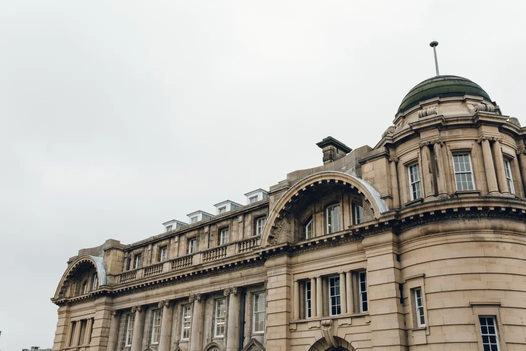 Grand Victorian stone building with domed tower and arched windows under overcast sky.