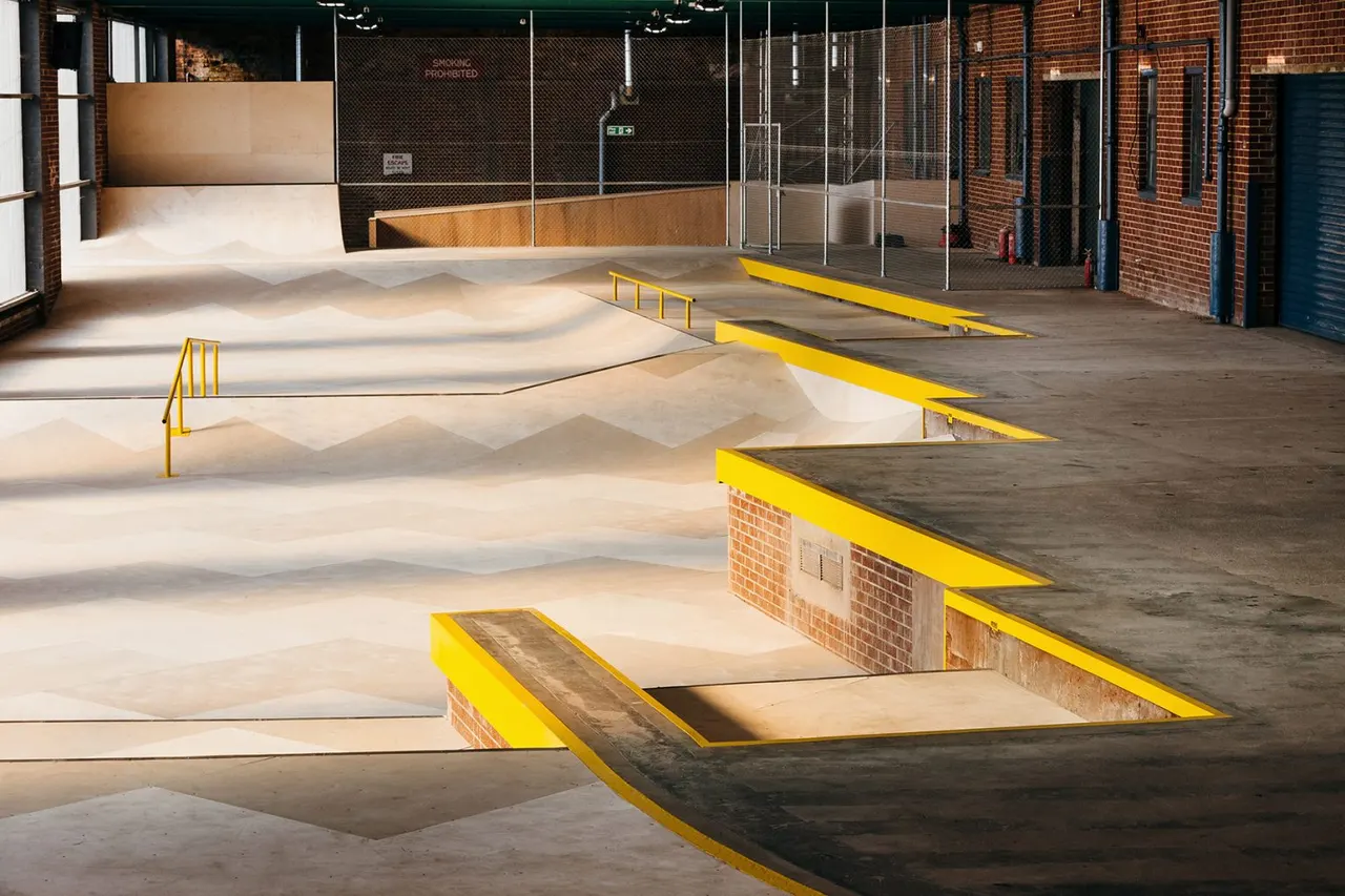 Indoor skate park with concrete bowls, ramps, and yellow-edged features in a brick warehouse.