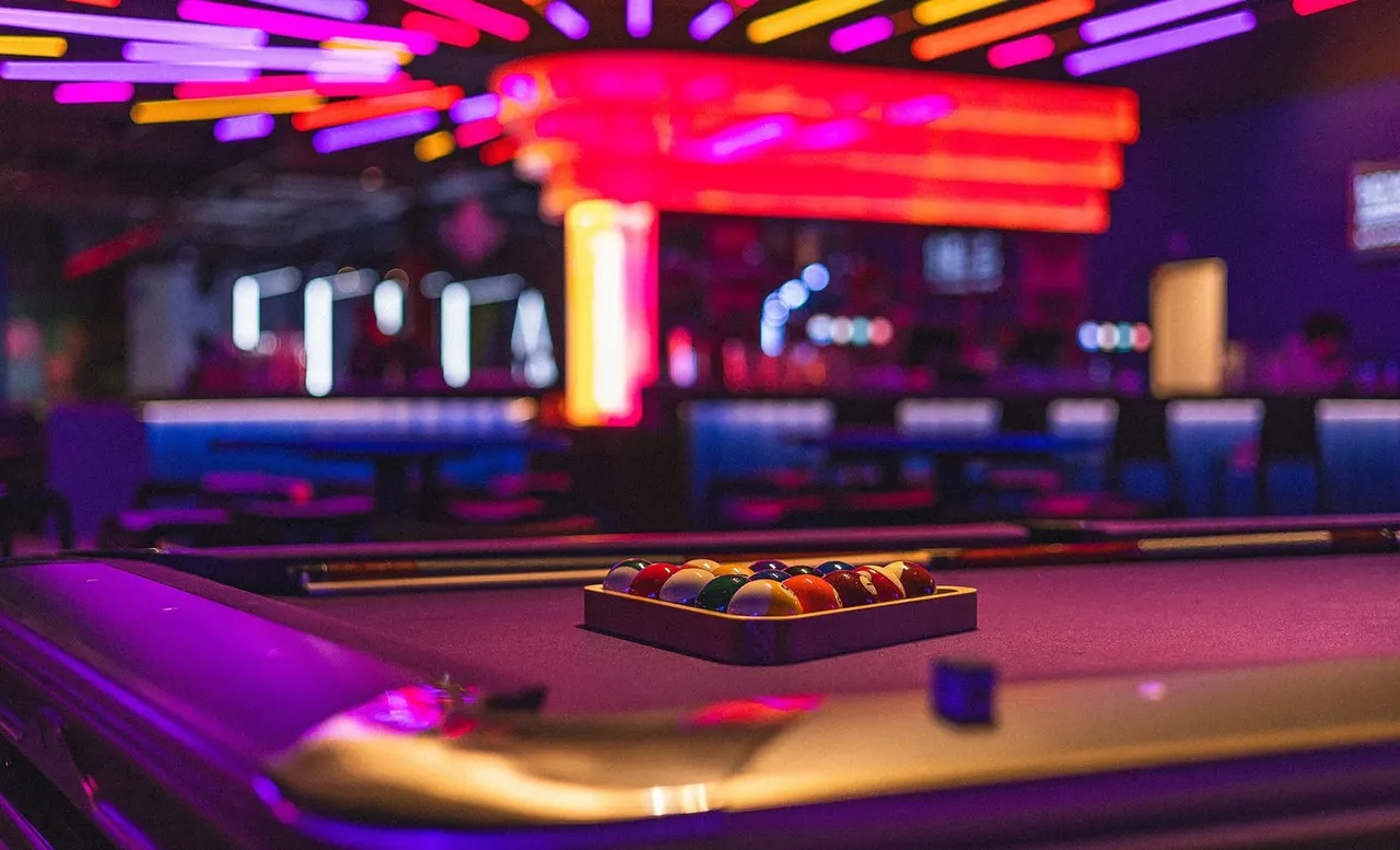 Coloured billiard balls arranged on a pool table in a neon-lit bowling alley.