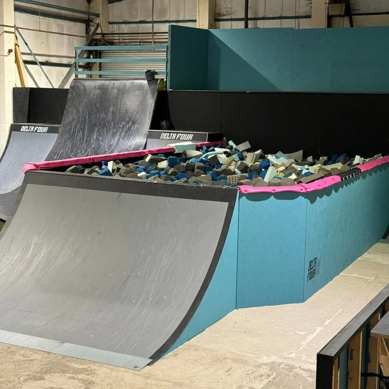 Indoor skate park with ramps and foam pit filled with coloured foam blocks.