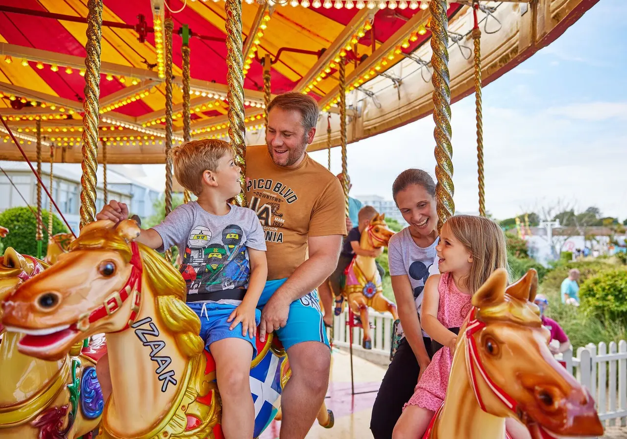 Family riding a colourful carousel with illuminated horses under a red and gold canopy.