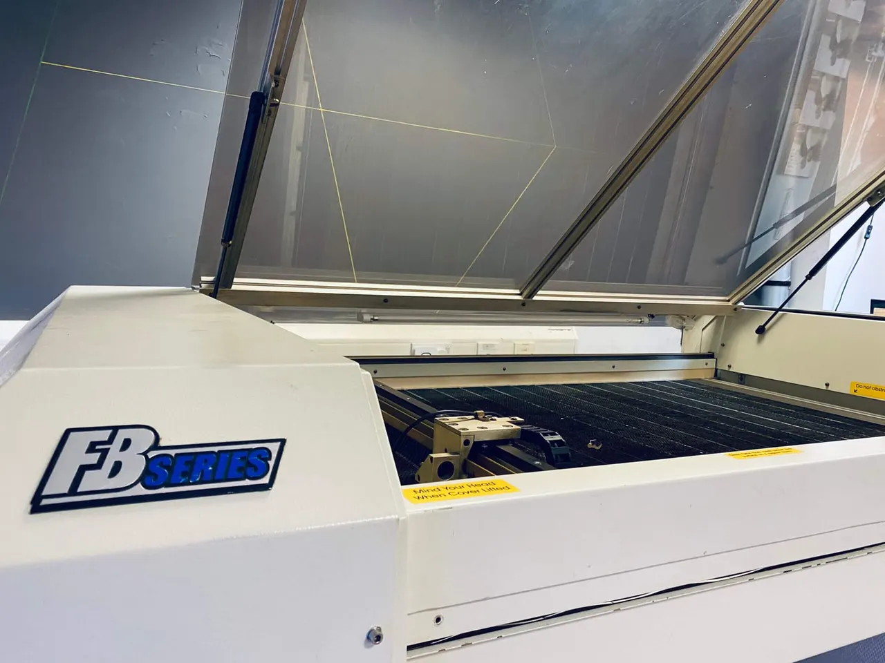 Opened laser cutter machine with translucent cover showing the cutting bed inside.