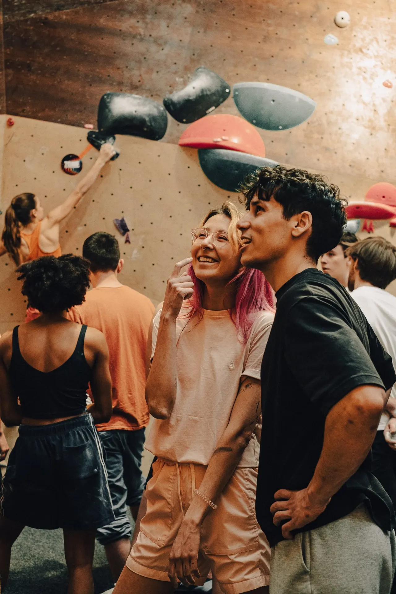 A group of young people smiling together indoors at an indoor climbing wall facility with coloured climbing holds.