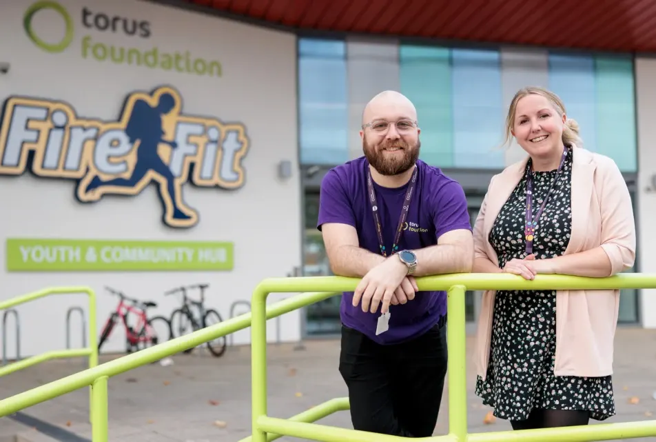 Two staff members lean against a lime-green railing outside the Torus Foundation FireFit youth centre building.