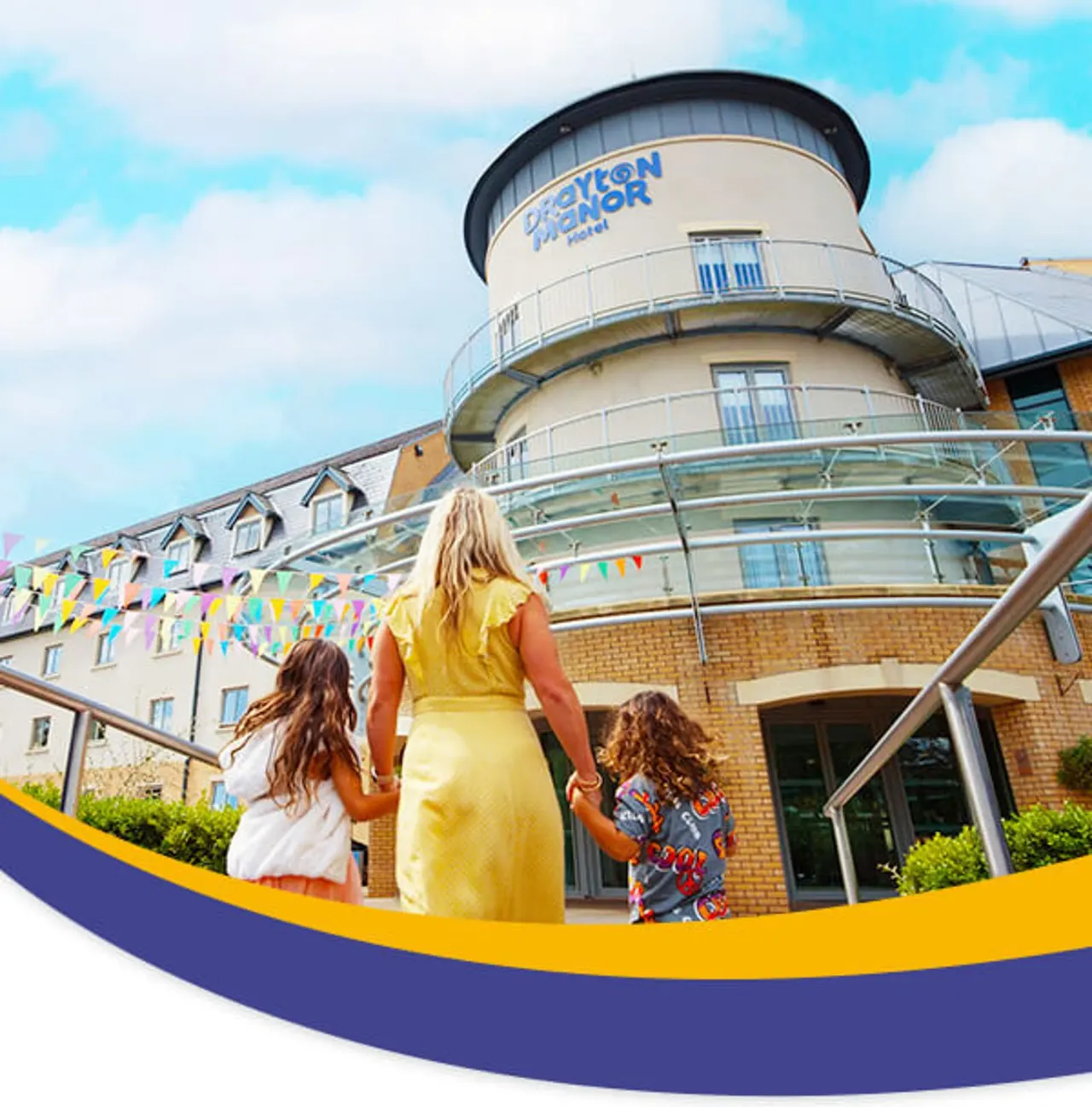 An adult and two children in casual clothing stand outside a modern cylindrical hotel building with colourful bunting decorations.