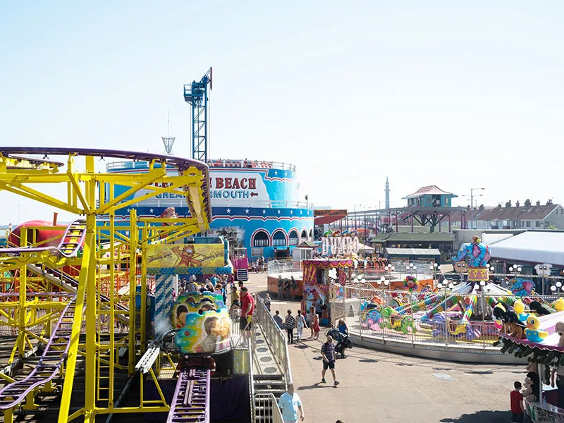 Busy amusement park with yellow roller coaster, colourful rides, and visitors enjoying the seaside arcade.