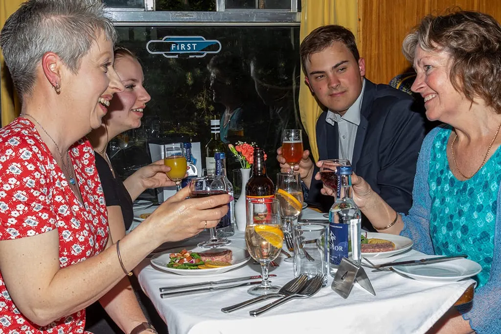 Four people dining together at a table with drinks and plated food in an elegant dining car.