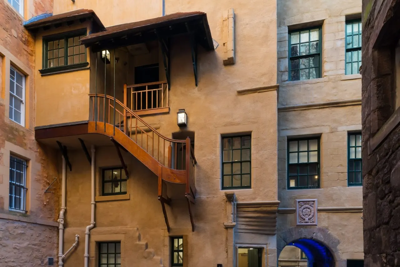 Historic stone buildings with external wooden staircase in a narrow Edinburgh cobbled courtyard.