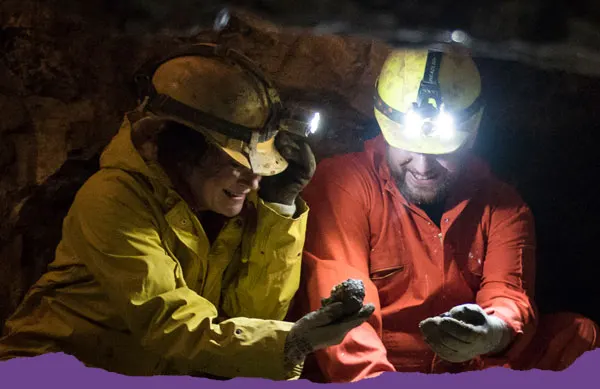 Two visitors wearing headlamps examine cave formations whilst caving underground.