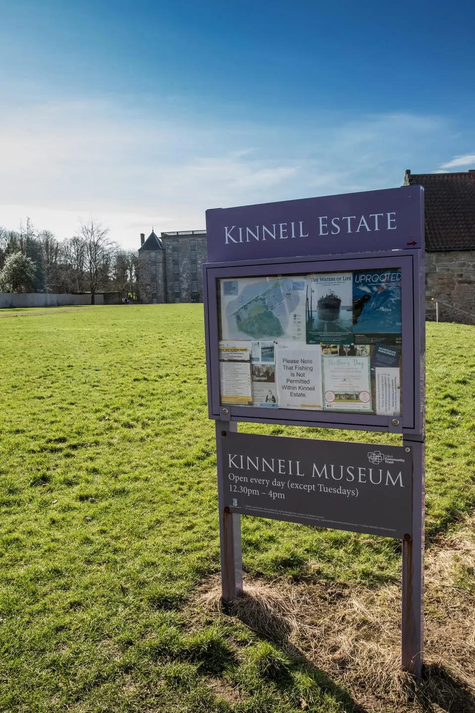 An information sign for Kinneil Estate and Museum stands in a green field with a historic stone tower house visible in the background.